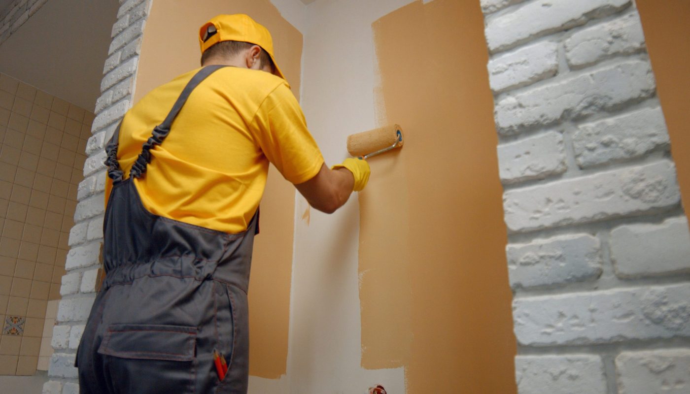 Worker painting wall with paint roller. Worker painting wall with paint roller. Builder paints the wall in brown color. Building, renovation and people concept.